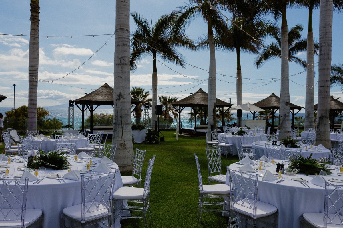 Reception tables with white linen under palm trees and string lights
