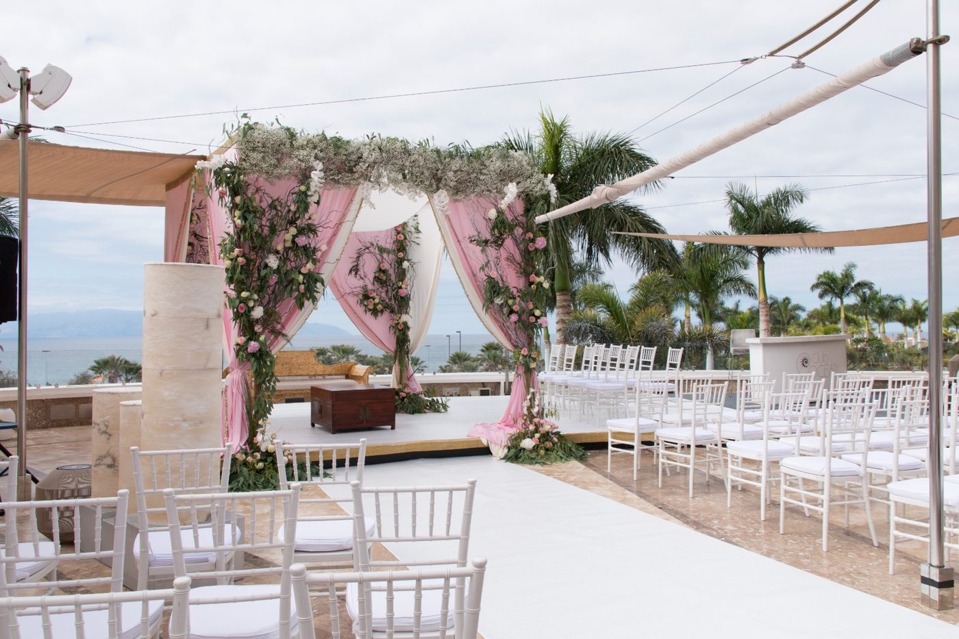 Wedding ceremony set-up with a floral arch and white chairs on a terrace overlooking the sea